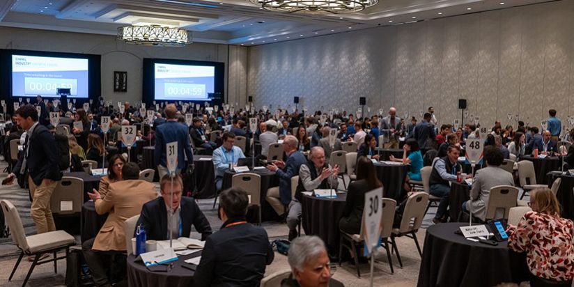 Hundreds of people sit at small tables in one-on-one meetings in a large ballroom.