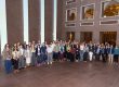 A group of 60 people in business dress pose in a large indoor lobby.