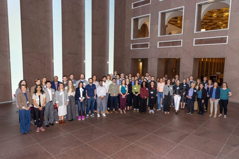 IN2 Channel Partner Meeting A group of 60 people in business dress pose in a large indoor lobby.