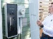 A man holds the cover of a power panel next to the panel hanging on the outside of a home.