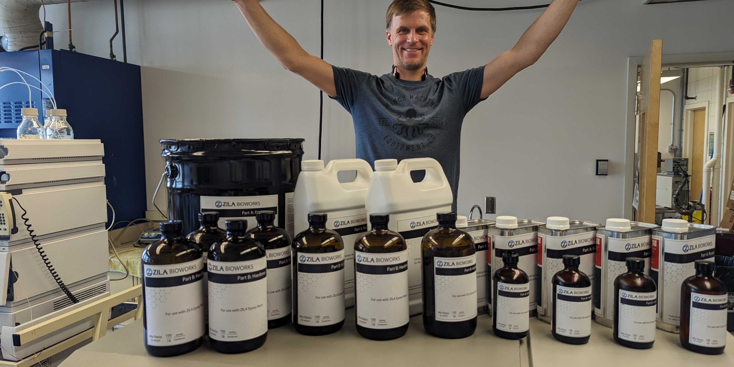 Evan raises his arms, palms down, over a collection of containers with the name, “Zila Bioworks” written on them.
